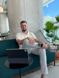 Dhiego Bento sentado em sum sofá verde, com um computador e o celular na mão